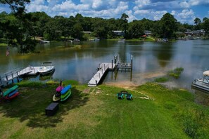A lakeside dock with boats and kayaks, surrounded by greenery and houses in the background. - Lake Days & Cozy Nights | Lake Murray Getaway (Lexington)