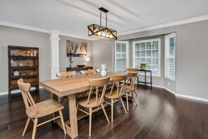 A dining area with a wooden table and chairs, a bookshelf, and a painting on the wall. - Lake Days & Cozy Nights | Lake Murray Getaway (Lexington)