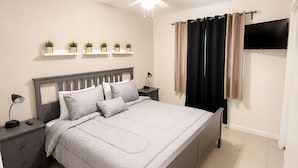 A bedroom with a bed, bedside tables, a ceiling fan, a TV, and a window with curtains.
