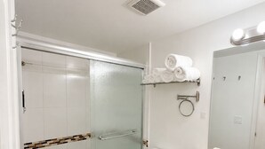 A bathroom with a glass-enclosed shower, a toilet, a sink with a mirror, and a towel rack with folded towels.