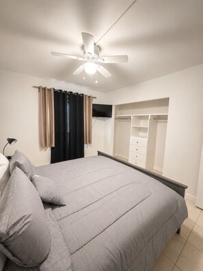 Een slaapkamer met een bed, een plafondventilator, een kledingkast en een spiegel.