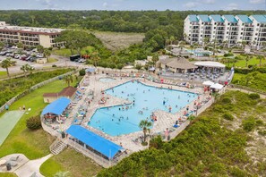 A large outdoor swimming pool surrounded by lounge chairs and umbrellas, with a parking area and buildings in the background. - Hilton Head Beach & Tennis Resort , Oceanfront, Tennis, Restaurants, Pickleball! (Hilton Head Island)