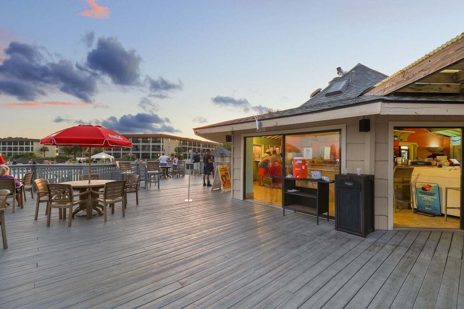Une terrasse extérieure avec un plancher en bois, des tables et des chaises, et un bâtiment doté d’une façade en verre.