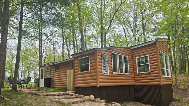 A log cabin with a stone pathway leading to the entrance, surrounded by trees.