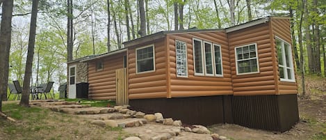 A log cabin with a stone pathway leading to the entrance, surrounded by trees.