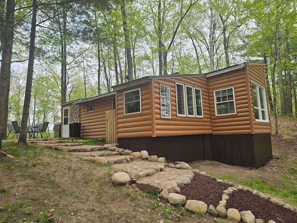 A log cabin with a stone pathway leading to the entrance, surrounded by trees.