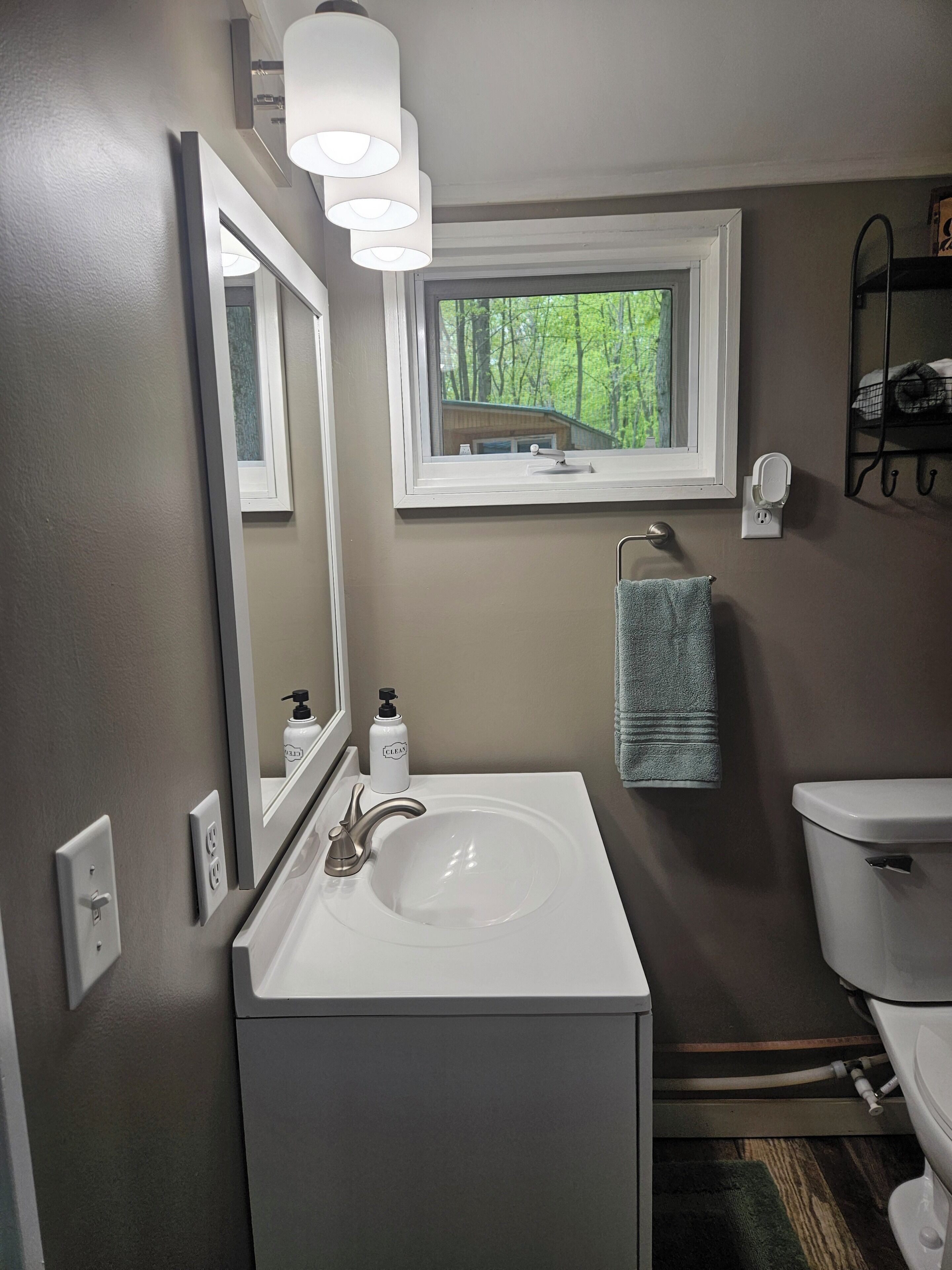 Une salle de bain avec un lavabo blanc, un miroir, une fenêtre et un porte-serviettes.