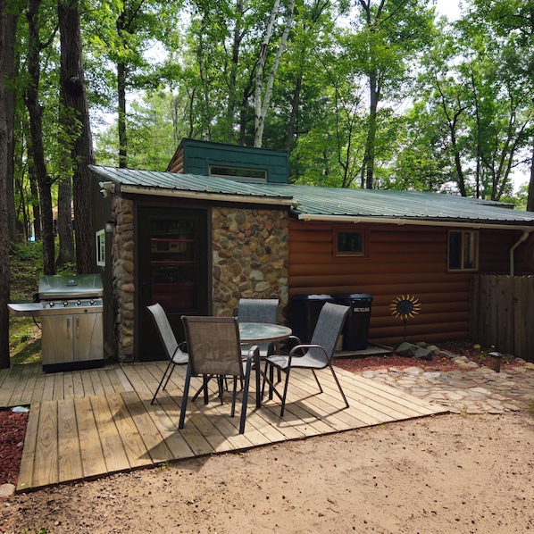 Una cabaña rústica con fachada de piedra, una parrilla y un patio con mobiliario exterior.
