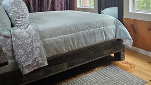 A bedroom with a wooden bed frame, a large window with a view of trees, and a ceiling with exposed beams.