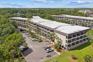 A multi-story hotel with a flat roof, surrounded by greenery and a parking lot. - Ocean Views | Community Pool, 2 BR, Sleeps 6, Walkable to Coligny Plaza! (Hilton Head Island)