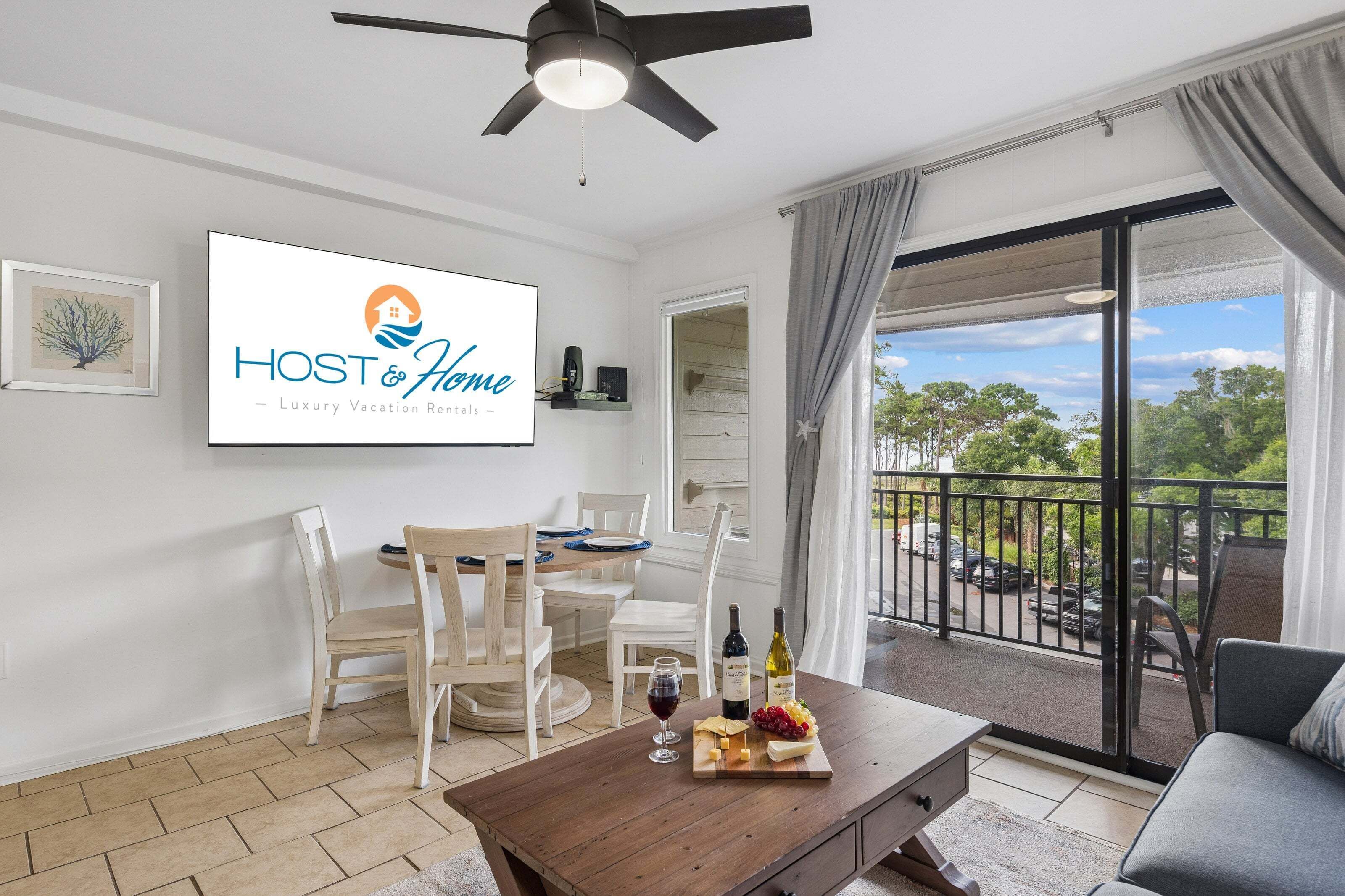 Ein modernes Wohnzimmer mit Essbereich, einem Schild mit der Aufschrift 'HOST & Home Luxury Vacation Rentals' und einem Balkon mit Blick.