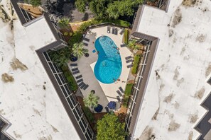 An aerial view of a swimming pool surrounded by lounge chairs and umbrellas, with a clear sky above. - Ocean Views | Community Pool, 2 BR, Sleeps 6, Walkable to Coligny Plaza! (Hilton Head Island)