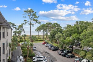 A parking lot with multiple cars, surrounded by trees and a building with a sloped roof. - Ocean Views | Community Pool, 2 BR, Sleeps 6, Walkable to Coligny Plaza! (Hilton Head Island)