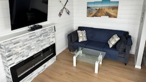 A living room with a flat-screen TV, a fireplace, a blue sofa, and a glass coffee table. - Bayfront! 2 BR/2 BA Upper condo [2nd/top floor]- Spectacular Bay view! [no dogs] (Brigantine)