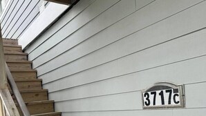 A wooden staircase leading to a house with a white siding exterior. A house number plaque is visible on the wall. - Bayfront! 2 BR/2 BA Upper condo [2nd/top floor]- Spectacular Bay view! [no dogs] (Brigantine)