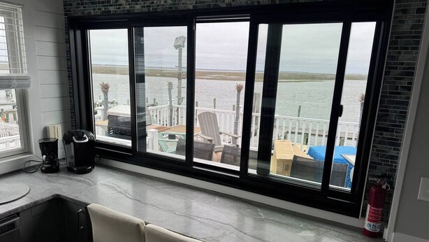 A room with a large window overlooking a body of water, a coffee maker, and a chair. - Bayfront! 2 BR/2 BA Upper condo [2nd/top floor]- Spectacular Bay view! [no dogs] (Brigantine)