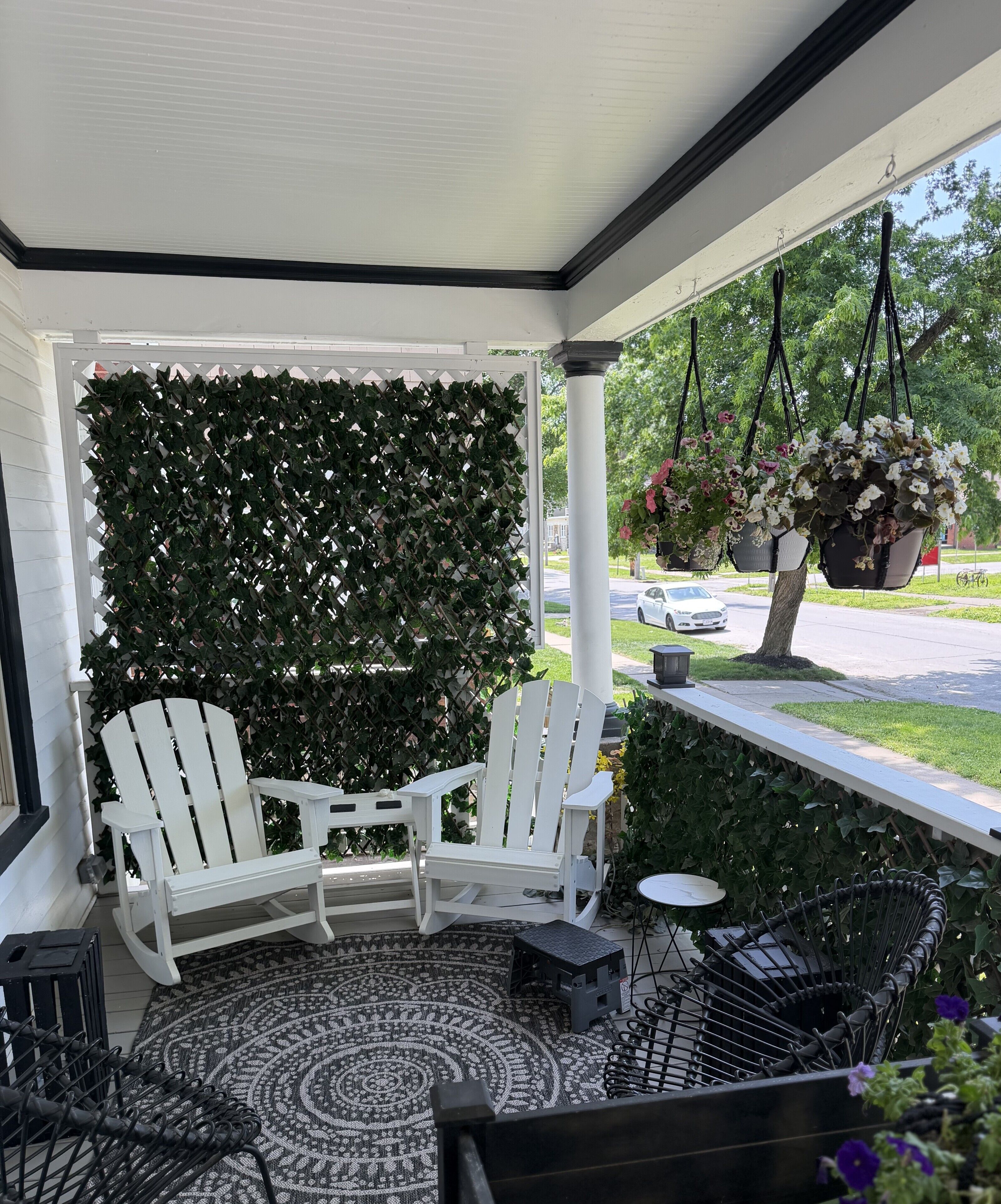 A porch with a white chair, a small table, and a hanging planter with flowers.