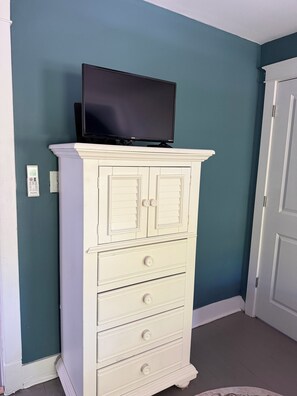 Un mueble blanco con un televisor de pantalla plana encima, frente a una pared verde azulado.