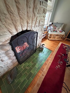 A fireplace with a decorative screen, a green tiled floor, a red rug, and a wooden cabinet with various items. - The Front Porch Bed and Breakfast (Excelsior Springs)