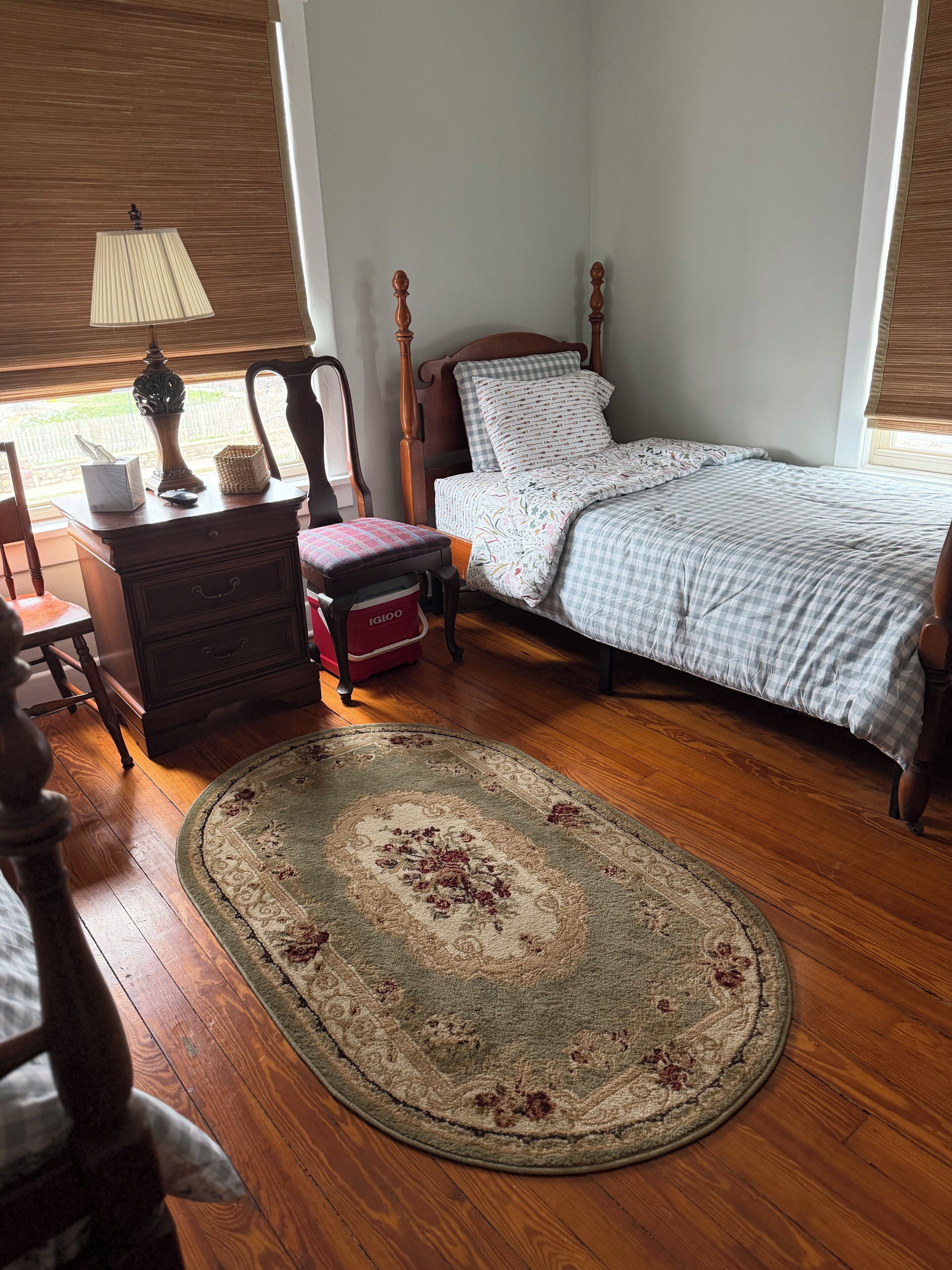 A bedroom with a wooden bed, a nightstand, a chair, a bedside table with a lamp, and a rug on the floor.