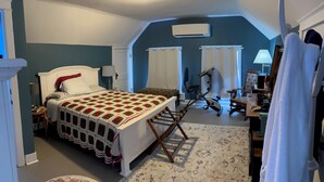 Un dormitorio con cama, escritorio, silla, bicicleta estática y ventana con cortinas.