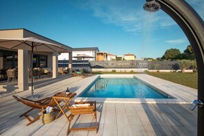 Uima-allas, jonka ympärillä on aurinkotuoleja ja pöytä. Allasta ympäröi puinen terassi ja katettu patioalue.