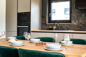 A modern dining area with a long wooden table set for a meal, green upholstered chairs, and a kitchen in the background. - Villa Casa Dvori (Istria - Valtura) (Valtura)