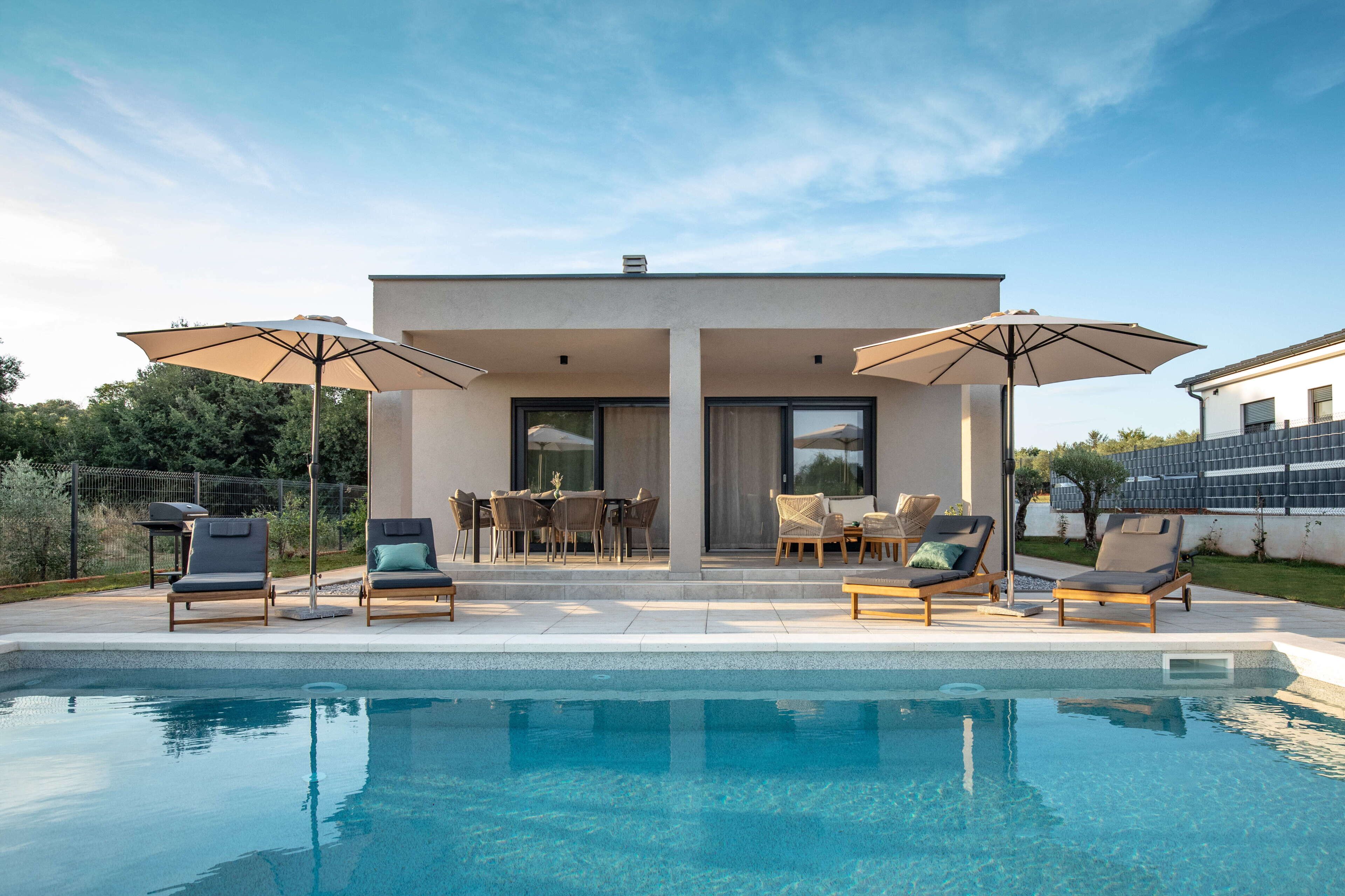 A modern house with a pool, outdoor seating, and umbrellas.