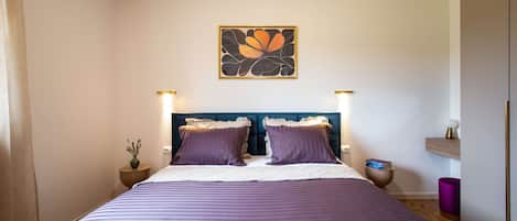A bedroom with a bed, two bedside tables, a nightstand, a wall-mounted artwork, and a bedside lamp.