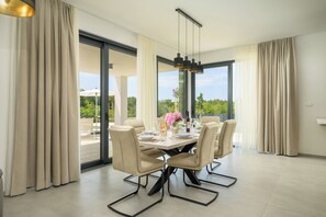 Ein Essbereich mit einem Tisch für sechs Personen, großen Fenstern und Blick auf Grünflächen.