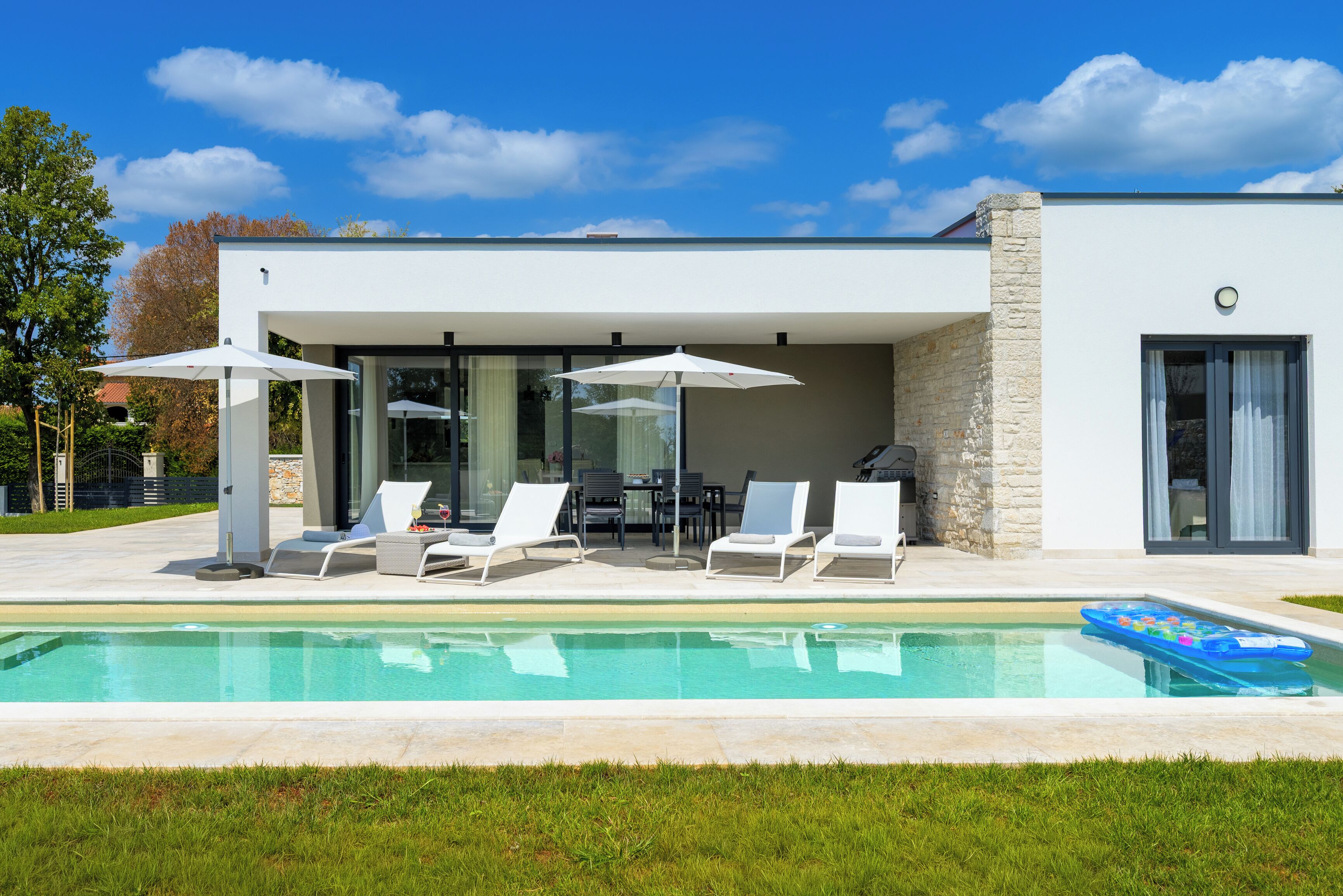 A modern house with a swimming pool, outdoor seating, and a covered patio area.