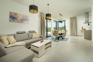 A modern living room with a sofa, coffee table, and dining area with chairs. There is a painting on the wall and a kitchen area visible in the background. - Villa Luen (Istria - Cukrići) (Cukrići)