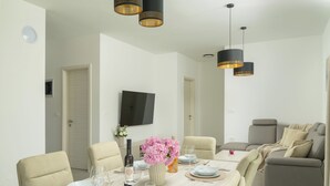 A dining area with a table set for four, chairs, a television mounted on the wall, and a sofa in the background. - Villa Luen (Istria - Cukrići) (Cukrići)