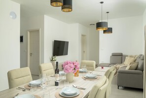 A dining area with a table set for four, chairs, a television mounted on the wall, and a sofa in the background. - Villa Luen (Istria - Cukrići) (Cukrići)