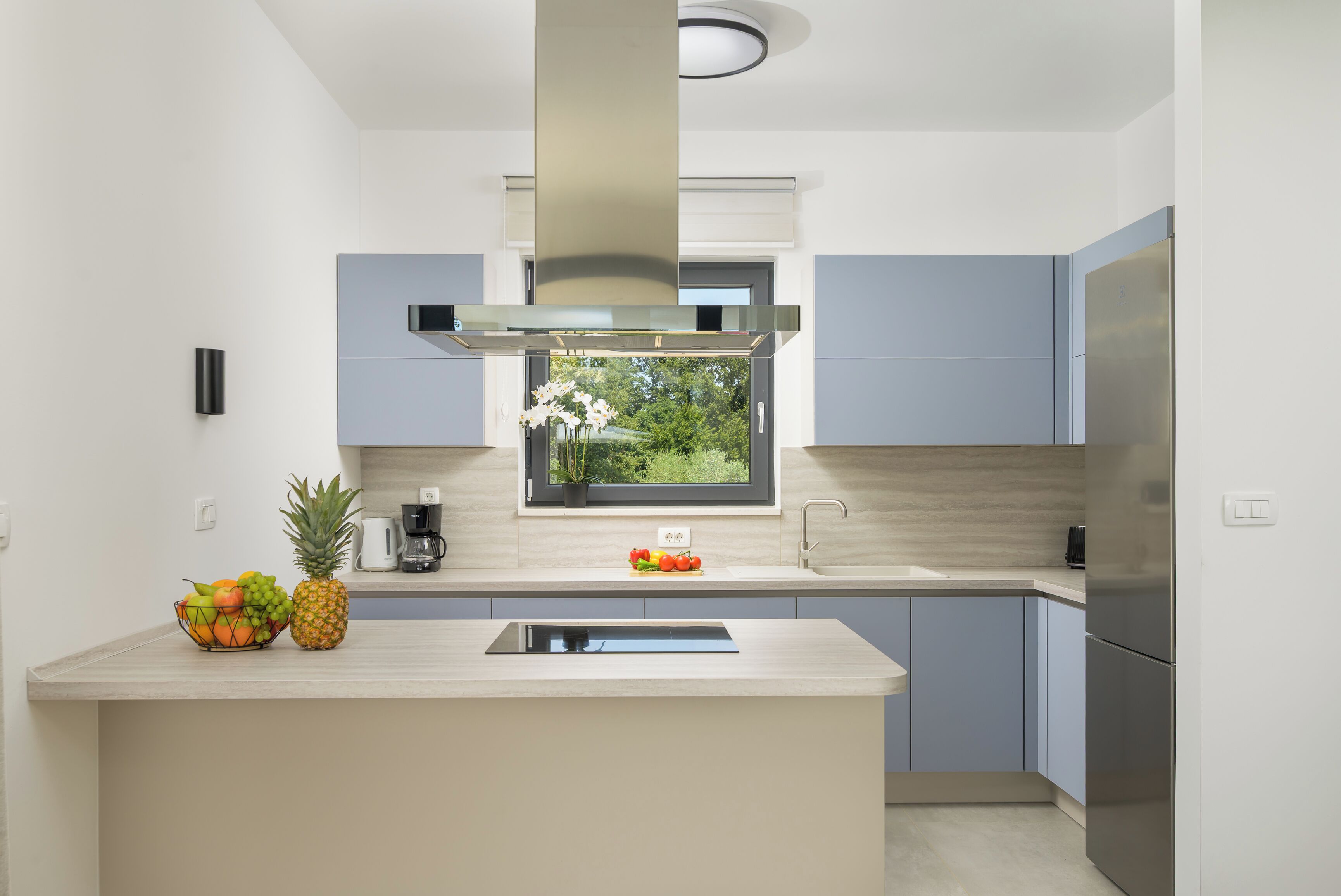 Una cocina moderna con una isla central, estufa integrada y ventana con vistas al verdor.
