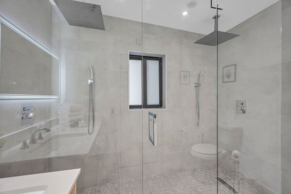 Ein modernes Badezimmer mit einer einbauartigen Spüle und einer großzügigen Dusche, die durch Glaswände abgegrenzt ist.
