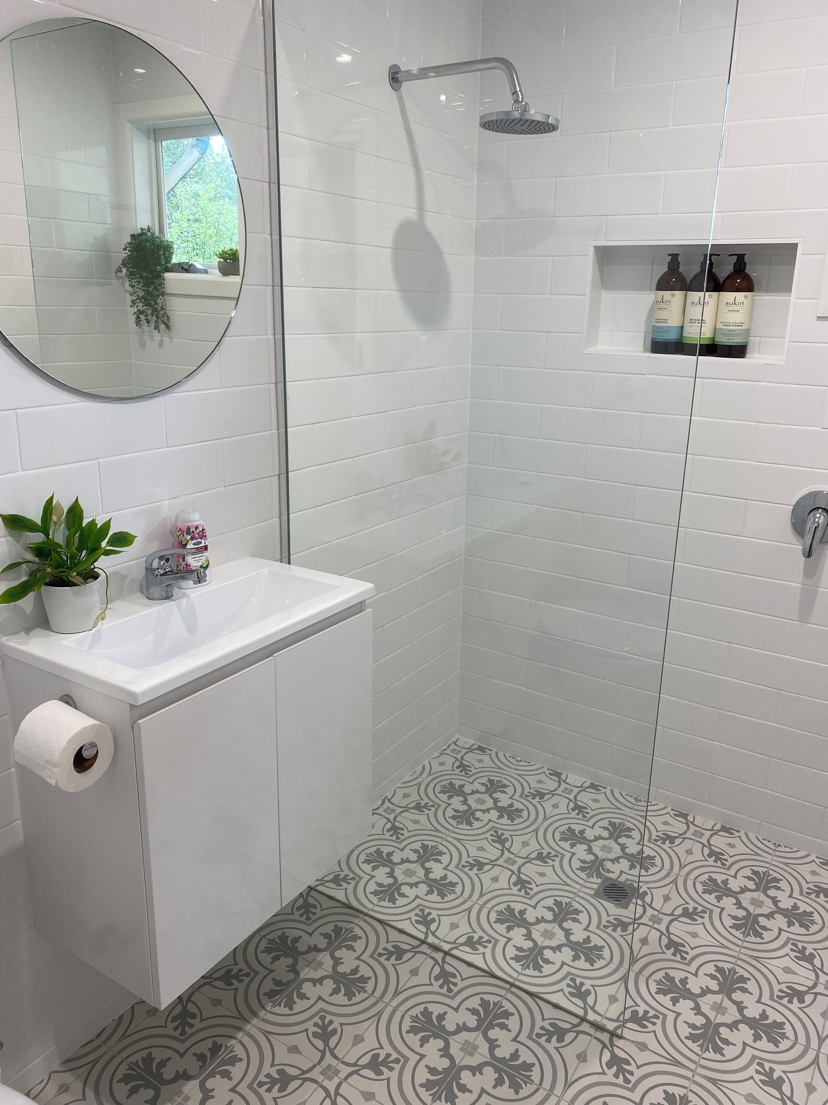 A bathroom with a shower, sink, mirror, and toiletries.