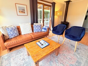 A living room with a brown leather sofa, two blue armchairs, a wooden coffee table, and a patterned rug. - Cosy Coastal Cottage in Red Rocks – Close to Beach & Phillip Island Attractions (Cowes)