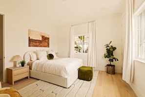 A bedroom with a bed, bedside table, lamp, and a potted plant.