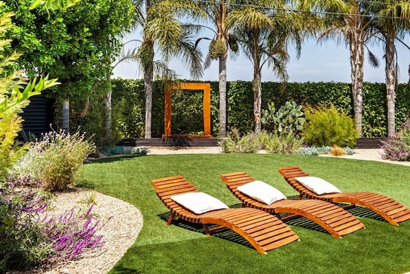 A garden with a wooden pergola, a lawn, and a seating area with lounge chairs.