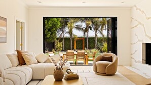 A modern living room with a sofa, armchair, coffee table, and a view of an outdoor patio with a dining set.