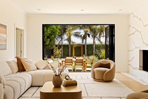 A modern living room with a sofa, armchair, coffee table, and a view of an outdoor patio with a dining set.