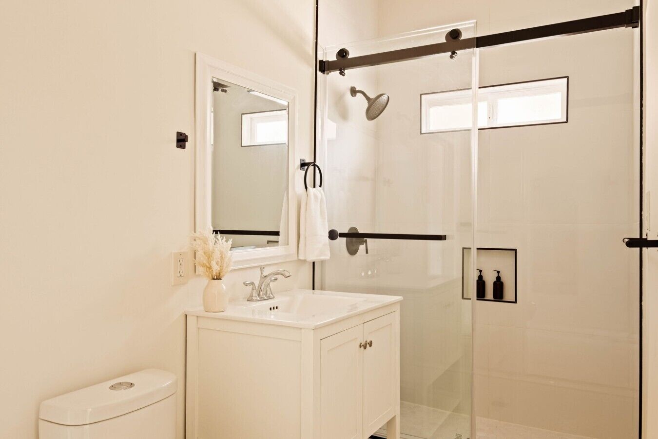 A modern bathroom with a glass shower enclosure, a white vanity, and a mirror.