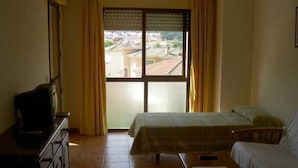 Habitación de hotel con cama, escritorio, televisor y vista a la ciudad a través de un ventanal grande.