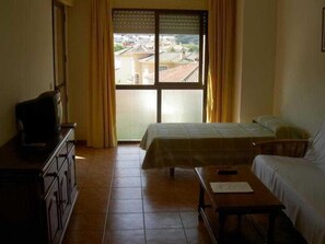 A hotel room with a bed, a desk, a television, and a view of the city through a large window. - Santa Clara (Alhaurin de la Torre)