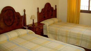 Una habitación con dos camas de madera, una mesita de noche con lámpara y una ventana con cortinas amarillas.