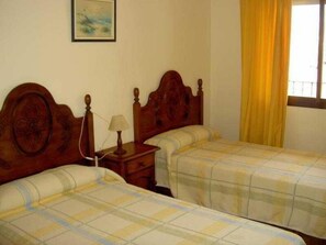 A room with two wooden beds, a nightstand with a lamp, and a window with yellow curtains. - Santa Clara (Alhaurin de la Torre)