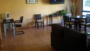 Habitación con televisión de pantalla plana montada en la pared, un escritorio con computadora, una silla, un sofá y una mesa de comedor con sillas.