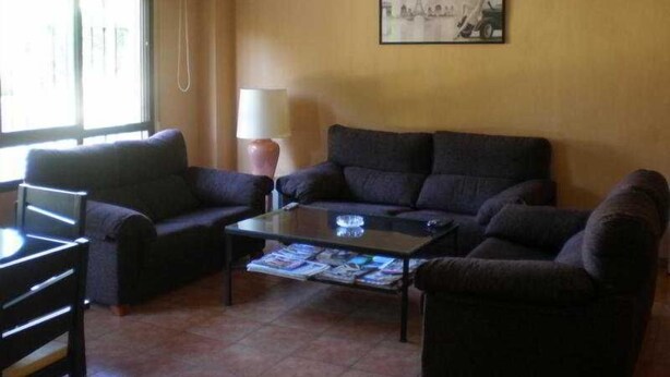 Una sala de estar con un juego de sofá, una mesa de centro con revistas, una lámpara y una ventana con cortinas.