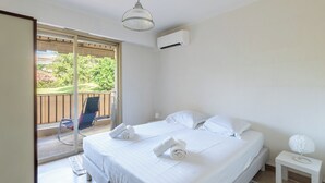 Ein Schlafzimmer mit einem Bett, Kissen, einem Nachttisch, einer Lampe und Blick auf einen Balkon mit einem Stuhl.